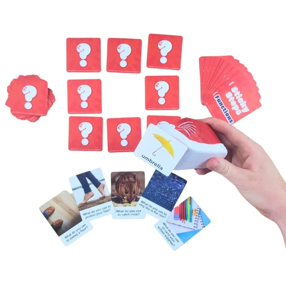 A hand holding a red and white card deck over a set of matching red question cards with white question marks, plus several illustrated cards spread out on a white background.