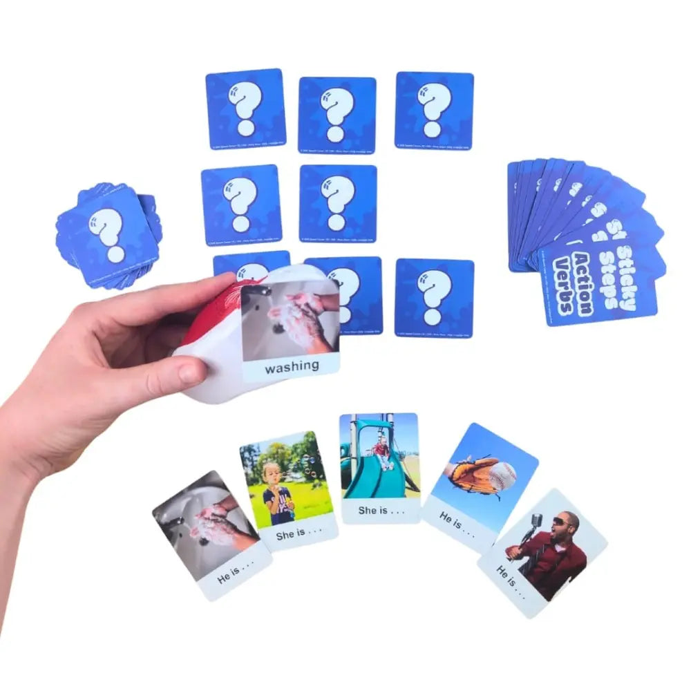 A hand holds a red and white card labeled 'washing' over a set of blue cards with question marks and text, with several sample cards fanned out below on a white background.