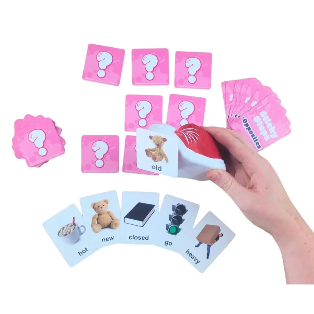 A hand holding a red and white card reader over a set of pink and white educational cards on a white background. The cards include question marks, opposites, and simple picture-based vocabulary words.