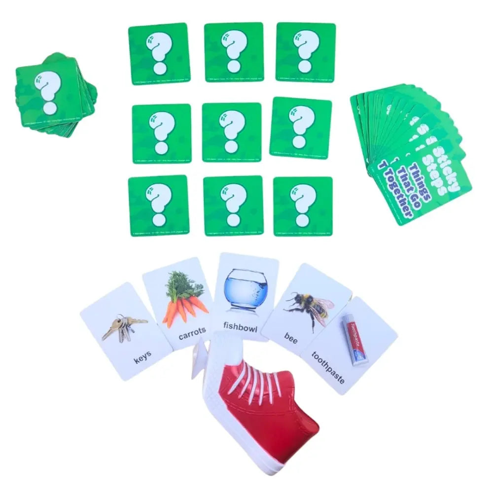 A children's educational card game set laid out on a white background, including green square cards with white question marks, a stack of green cue cards, and several white image cards showing illustrations and words such as keys, carrots, fishbowl, bee, and toothpaste. A red-and-white shoe illustration appears near the bottom.