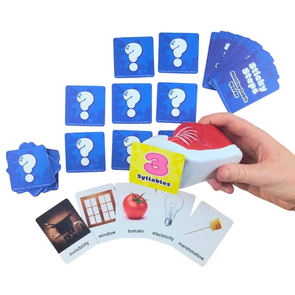 A hand holding a red and white card deck labeled 'Syllables' with a yellow card showing the number 3, surrounded by blue question-mark cards and white image cards on a white background.