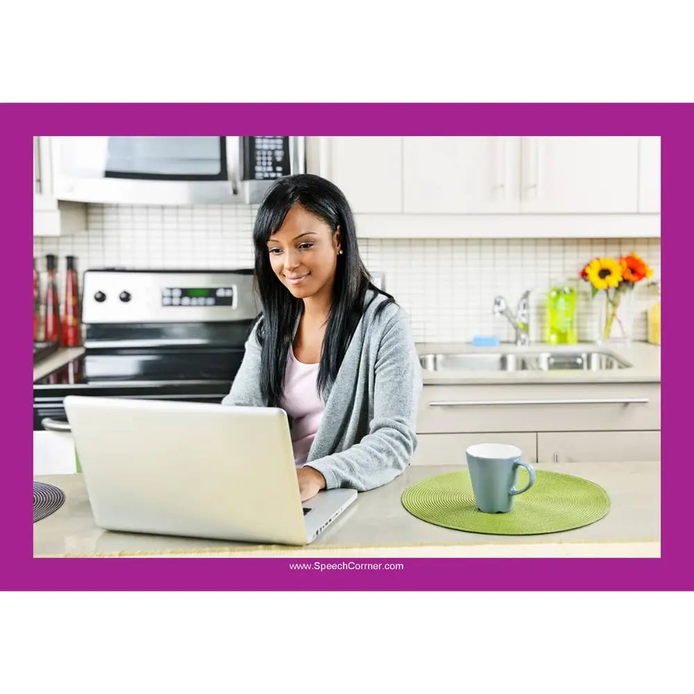 A woman with long dark hair sits at a kitchen counter using a laptop. She wears a gray cardigan over a light pink top.