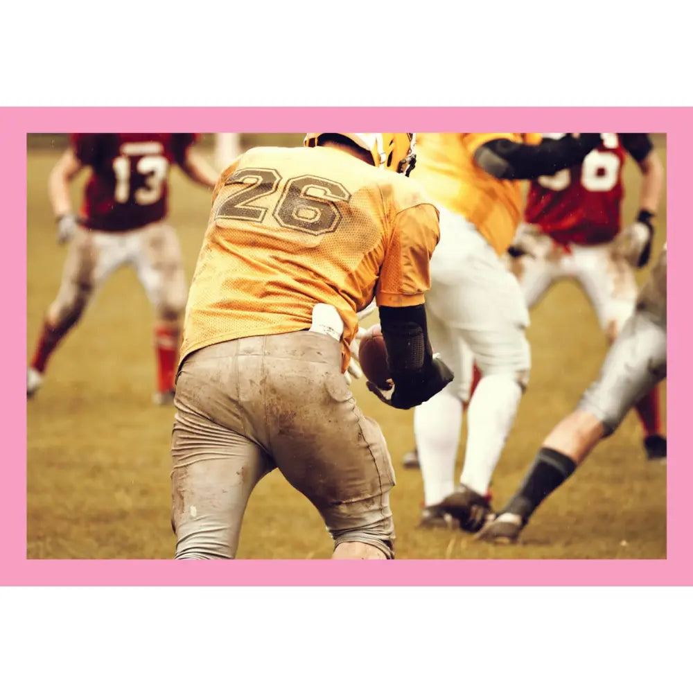 A football player in a yellow jersey with the number 26, viewed from behind, on a grassy field with other players blurred in the background. The photo is framed by a solid pink border.