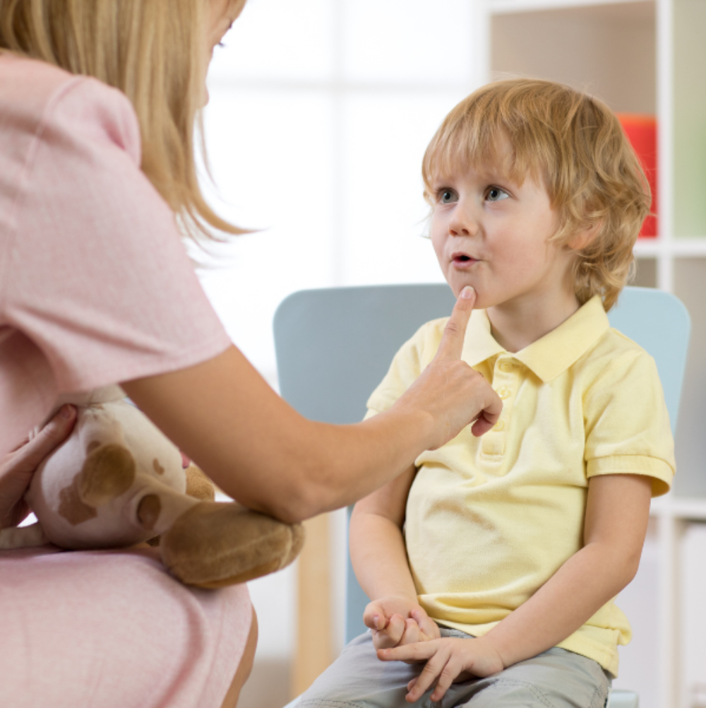 Young boy with blonde hair wearing a yellow shirt participating in a speech therapy lesson